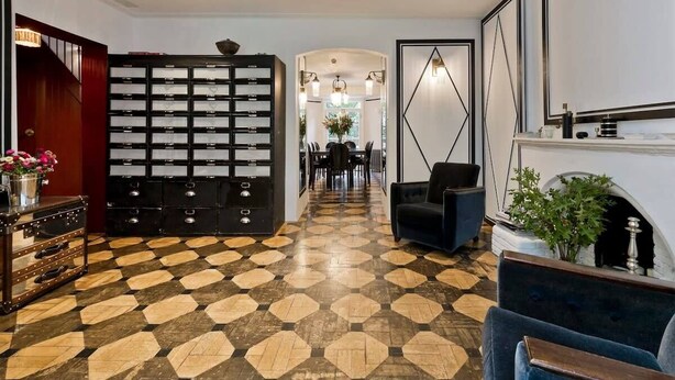 A hotel lobby with a check-in counter, a seating area with a sofa and armchairs, a patterned floor, and a decorative wall with a geometric design. - Stylish 5 Bed House in St. John's Wood/maida Vale (London)