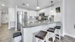 Una cocina moderna con armarios blancos, encimera de granito, electrodomésticos de acero inoxidable y taburetes de bar.