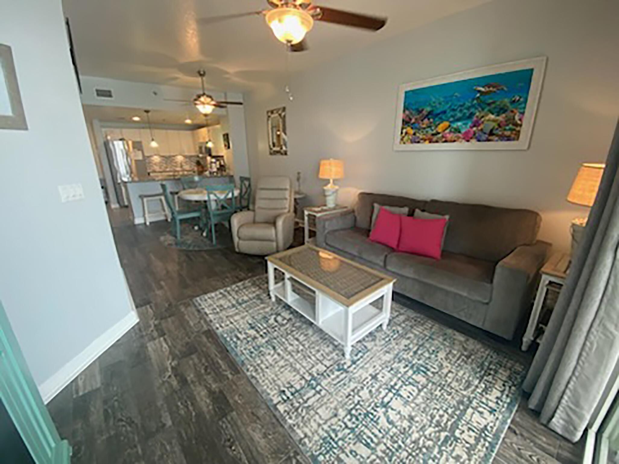 Un salon avec un canapé gris, une table basse et un tapis à motifs. Un tableau représentant une scène sous-marine est accroché au mur.