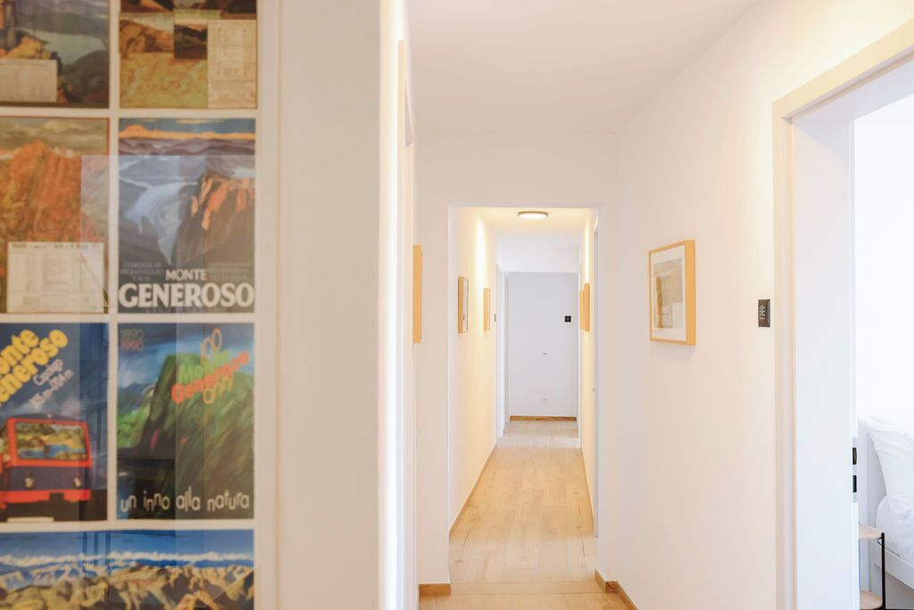 A hallway with a wooden floor, white walls, and framed pictures on the left.