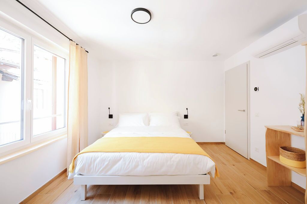 Un dormitorio minimalista con cama, mesitas de noche, una ventana y una puerta.