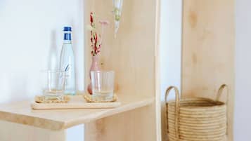 A wooden shelf with a clear glass bottle, a clear glass, and a pink vase with dried flowers.