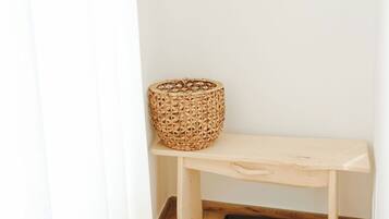 Un banco de madera con una cesta tejida a su lado, una bandeja negra en el suelo y un perchero de madera con ganchos.