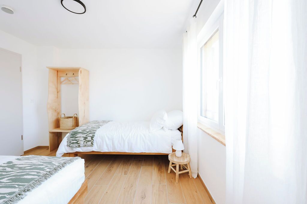 Ein Schlafzimmer mit einem Bett, einem Holzschrank, einem kleinen Tisch und einem Fenster mit Vorhängen.
