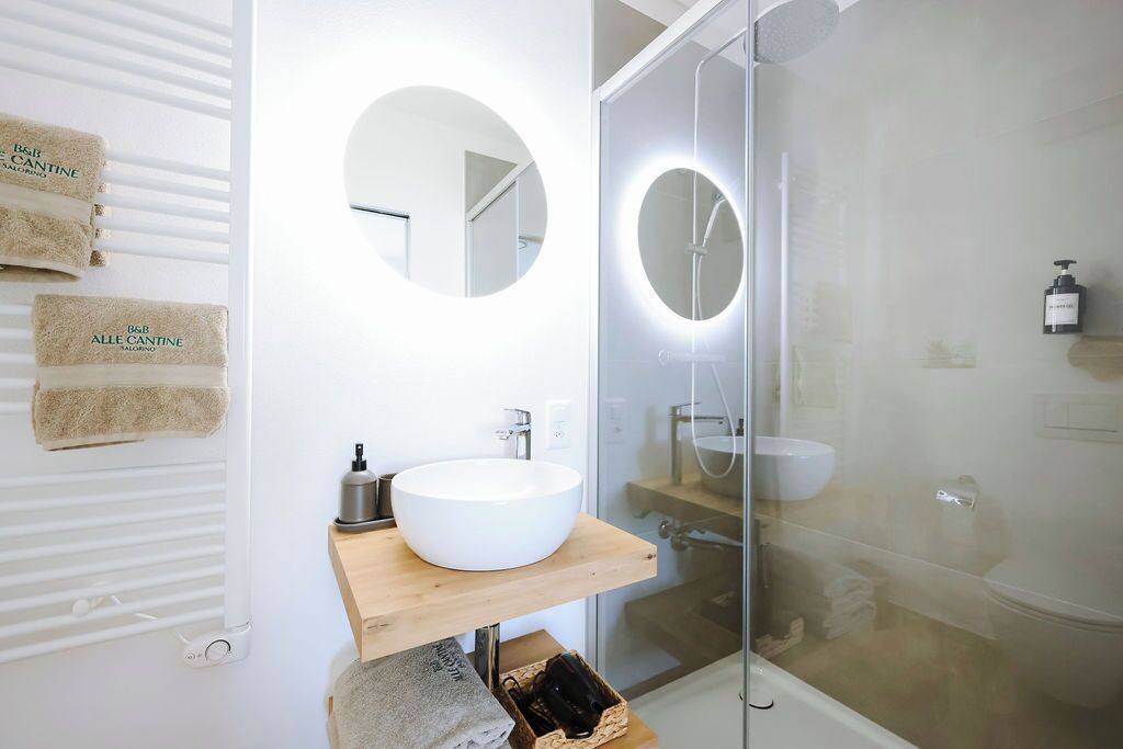 Casa de banho moderna com lavatório branco, espelhos redondos e cabine de duche em vidro.
