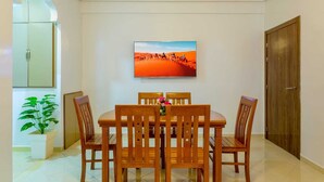 Un coin repas avec une table et des chaises en bois, un tableau représentant un paysage désertique, une plante en pot et un meuble.