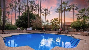 Une piscine à l’eau d’un bleu cristallin, entourée de palmiers et baignée par la lumière d’un coucher de soleil.