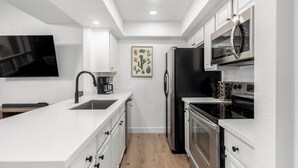Une cuisine moderne avec des meubles blancs, un réfrigérateur noir, un four à micro-ondes, une cuisinière et une machine à café.