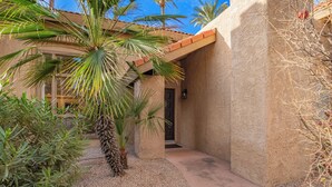 Un bâtiment aux murs recouverts d’enduit et doté d’un toit en tuiles, entouré de palmiers et d’un sol en gravier.