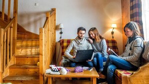 Un salon chaleureux avec un escalier en bois, un canapé, une table basse avec du matériel de tricot et un ordinateur portable.