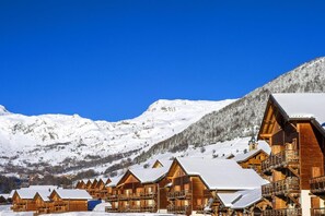 A row of wooden cabins with snow-covered roofs, set against a backdrop of snow-covered mountains and clear blue sky. - Swimming pool, sauna, balcony, parking, tv, ski locker, 36m², Saint Sorlin d'Arves (Saint-Sorlin-d'Arves)
