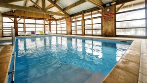 Une piscine intérieure avec des poutres en bois, de grandes fenêtres et un panneau indiquant une profondeur de 1,10 mètre.