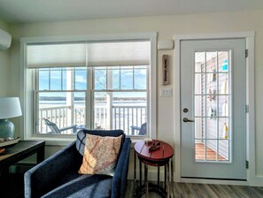 A room with a view of a dock, a chair with a map pillow, a small table with a fish, and a door with a grid pattern.