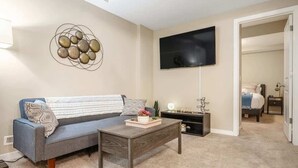 A living room with a sofa, coffee table, and a flat-screen TV mounted on the wall. - The Grande 1BD 1BA - Full Kitchen Guest Suite (Calgary)