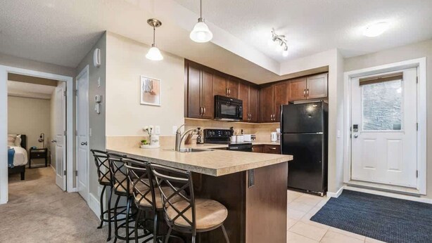 A modern kitchen with a central island, bar stools, and built-in appliances. - The Grande 1BD 1BA - Full Kitchen Guest Suite (Calgary)