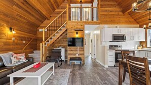 Ein großzügiger Loft-Wohnbereich mit Holzvertäfelung, einer Treppe zu einem Schlafloft, einer Küche mit weißen Schränken und einem Wand-Fernseher.
