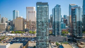 A cityscape with modern high-rise buildings, a parking lot, and a clear blue sky. - Miso 2 BD - Skyline View, Patio, Gym, Pool & AC (Calgary)