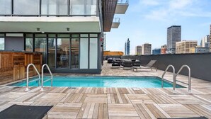 A rooftop pool with wooden decking, lounge chairs, and a city skyline in the background. - Miso 2 BD - Skyline View, Patio, Gym, Pool & AC (Calgary)