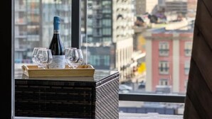 A bottle of wine and glasses on a tray by a window with a city view. - Miso 2 BD - Skyline View, Patio, Gym, Pool & AC (Calgary)