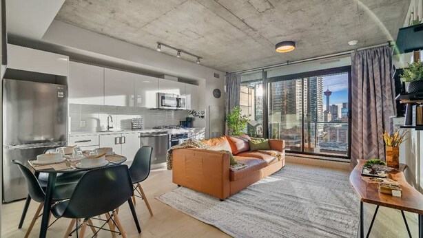 A modern apartment with a kitchen, dining area, and a large window with a city view. - Miso 2 BD - Skyline View, Patio, Gym, Pool & AC (Calgary)