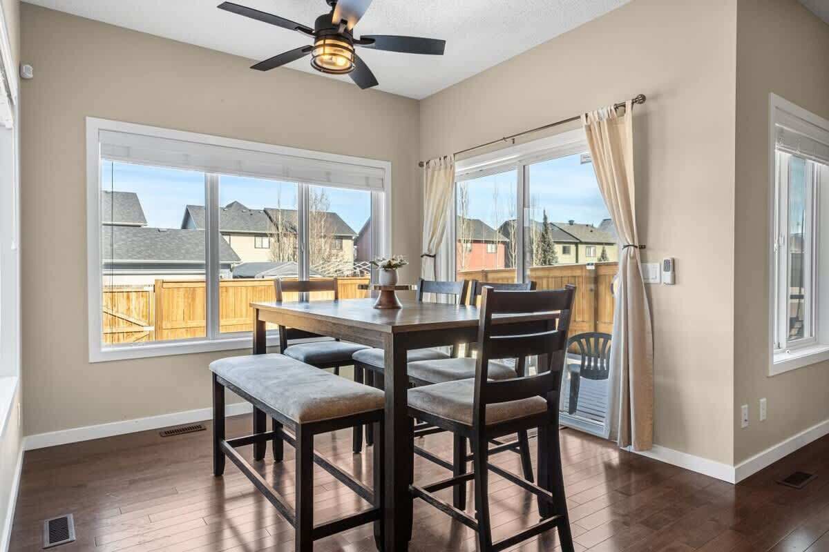 A dining area with a table and chairs, large windows, and a ceiling fan.