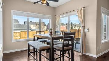 A dining area with a table and chairs, large windows, and a ceiling fan.