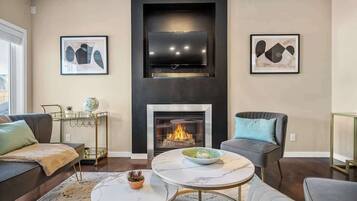 A modern living room with a fireplace, a mounted TV, and two framed abstract paintings.