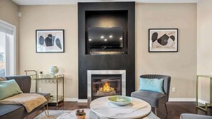 A living room with a fireplace, a flat-screen TV mounted above it, and two framed abstract paintings on the walls. - The Venti - 3BD 2BA Yard Garage & Upper Suite (Calgary)