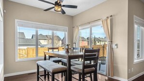 A dining area with a table and chairs, large windows, and a ceiling fan. - The Venti - 3BD 2BA Yard Garage & Upper Suite (Calgary)