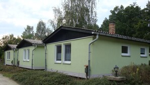 A row of green cottages with white window frames, a gravel path, and dense shrubbery. - Vacation cottage in the countryside approx. 150 m from the SpreewaldTherme-M (Burg (Spreewald))