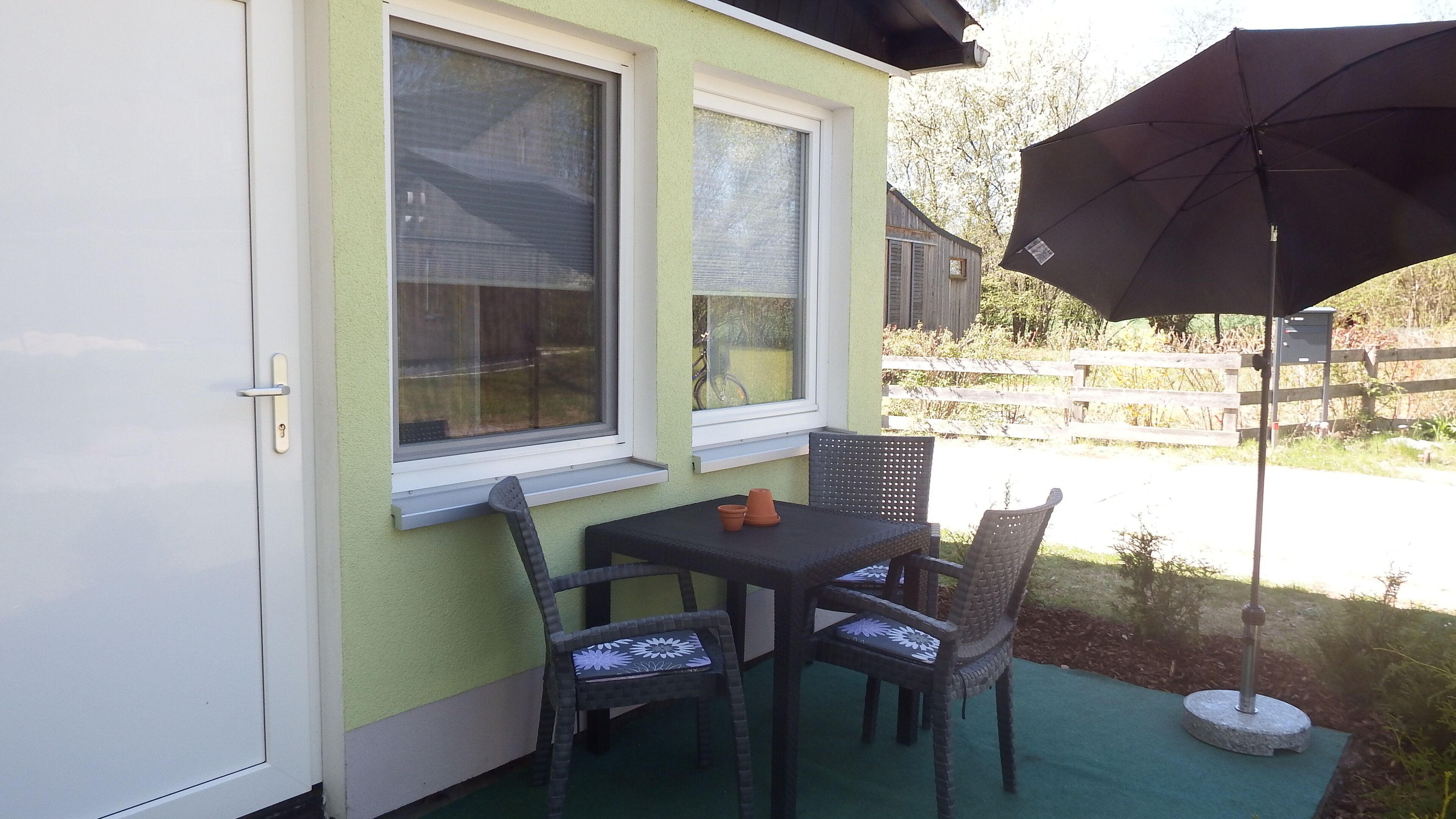 A patio with a table and chairs, a window, and a black umbrella.