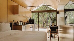 Un dormitorio moderno y minimalista con una cama grande, una pequeña kitchenette y vistas al bosque.