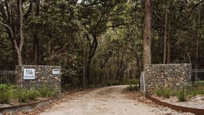 Un camino de tierra que atraviesa un área boscosa con muros de piedra y un letrero que dice '114 Myola Rd'.
