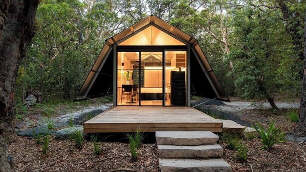 Una cabaña de madera moderna estilo A, con puerta de vidrio, rodeada de un bosque.