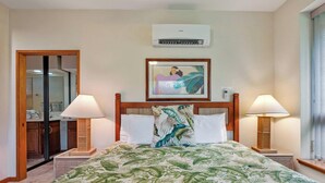 Hotelkamer met een bed, twee bedlampen, een foto in een lijst aan de muur, een airconditioning en een deur naar een badkamer.