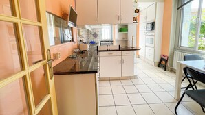 A kitchen with white cabinets, a black countertop, and a window with blinds. - L'Arpège du Puy - House* ParkingView * Family* 10min walk from Center (Le Puy-en-Velay)