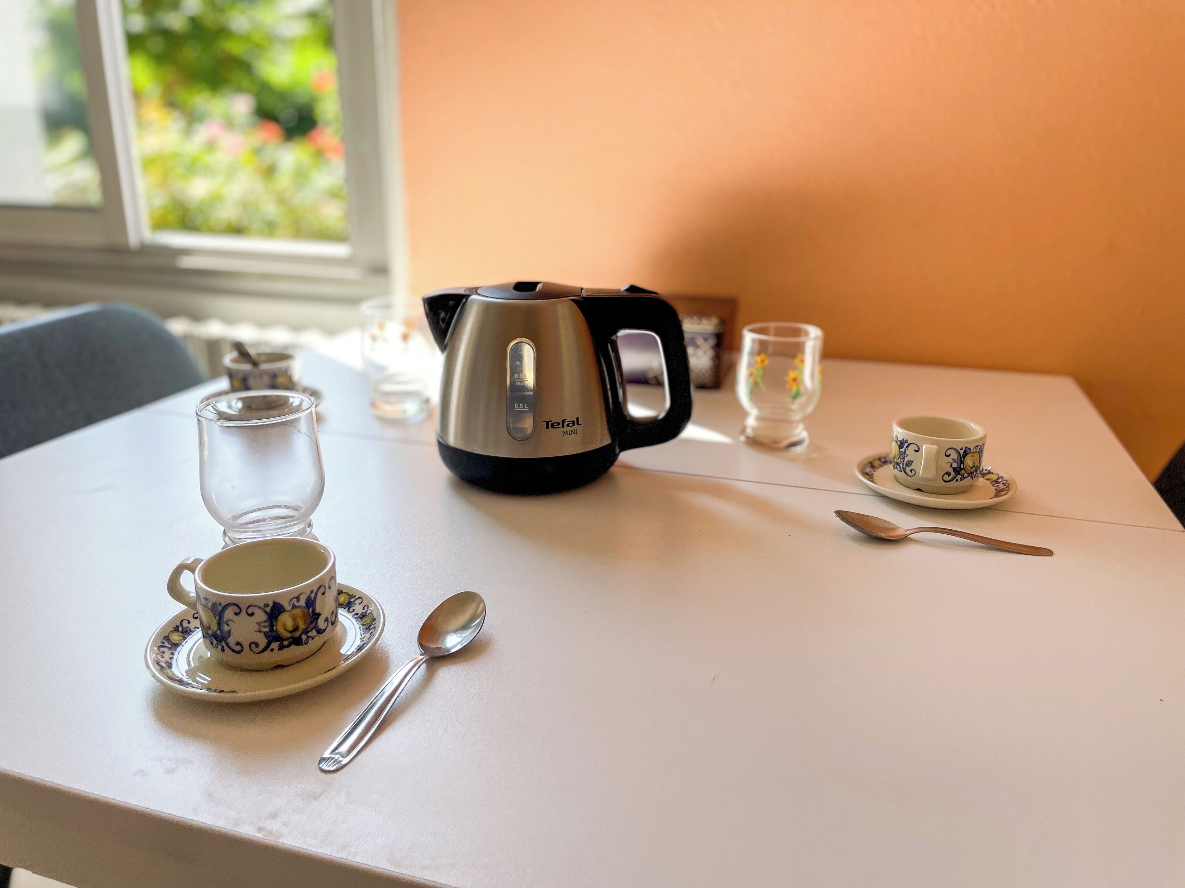 A table with a tea kettle, a cup, a saucer, a glass, and a spoon.
