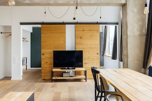 Ein modernes Wohnzimmer mit einem Holzboden-Fernseherstand, einem Esstisch und einem großen Fenster.