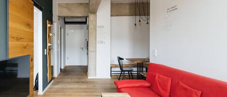 A modern living room with a red sofa, wooden flooring, a TV, and a dining area in the background.
