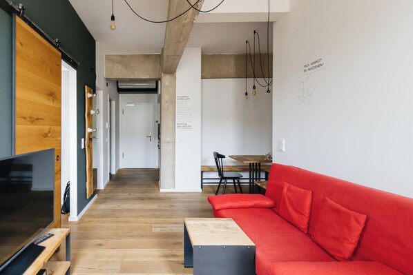 Una sala de estar moderna con un sofá rojo, piso de madera, un televisor y un comedor al fondo.
