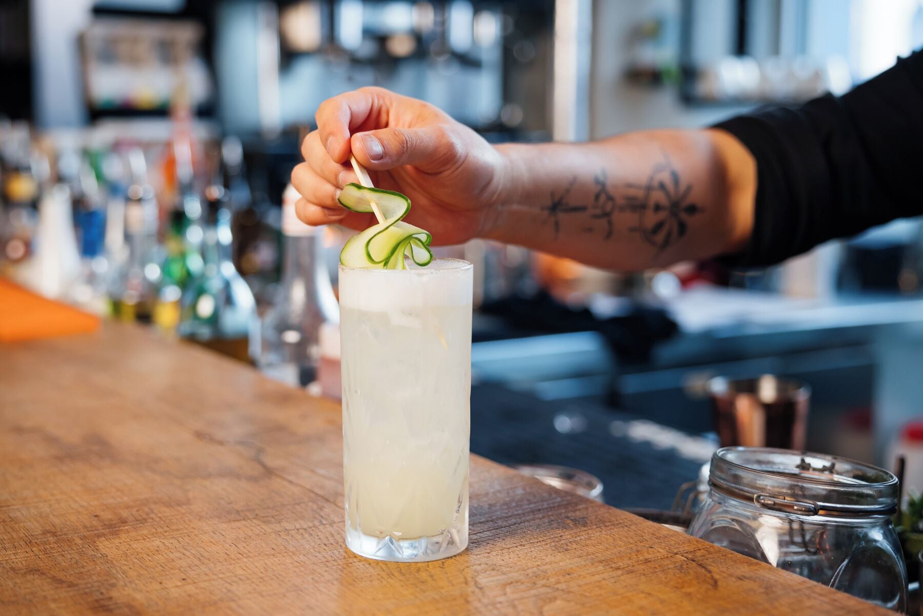 Ein Barkeeper dekoriert ein Getränk mit einer Gurkenscheibe und Schalotten.
