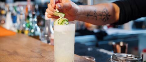 A bartender garnishing a drink with a cucumber slice and green onion.