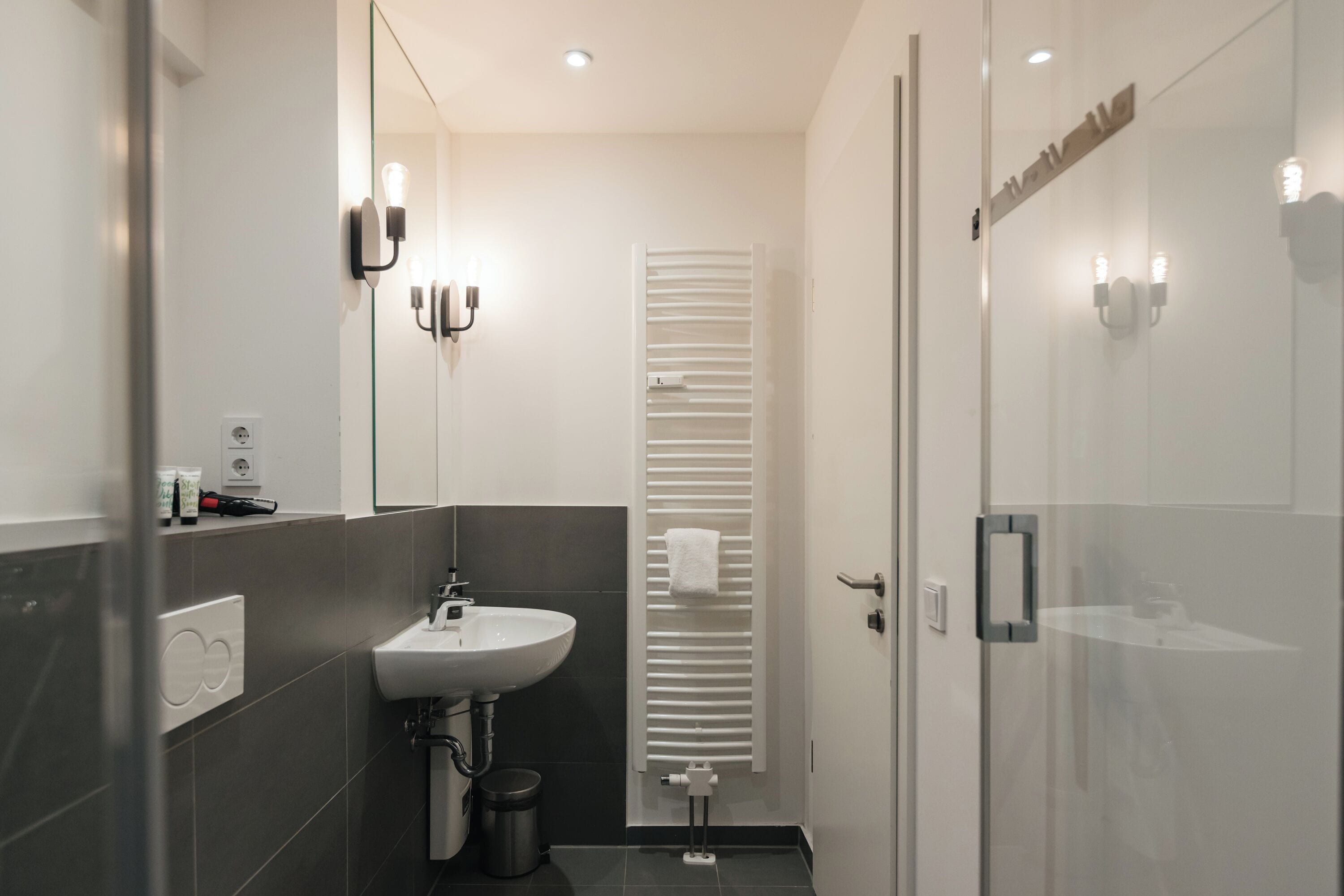 A modern bathroom with a sink, mirror, towel rack, and glass shower enclosure.