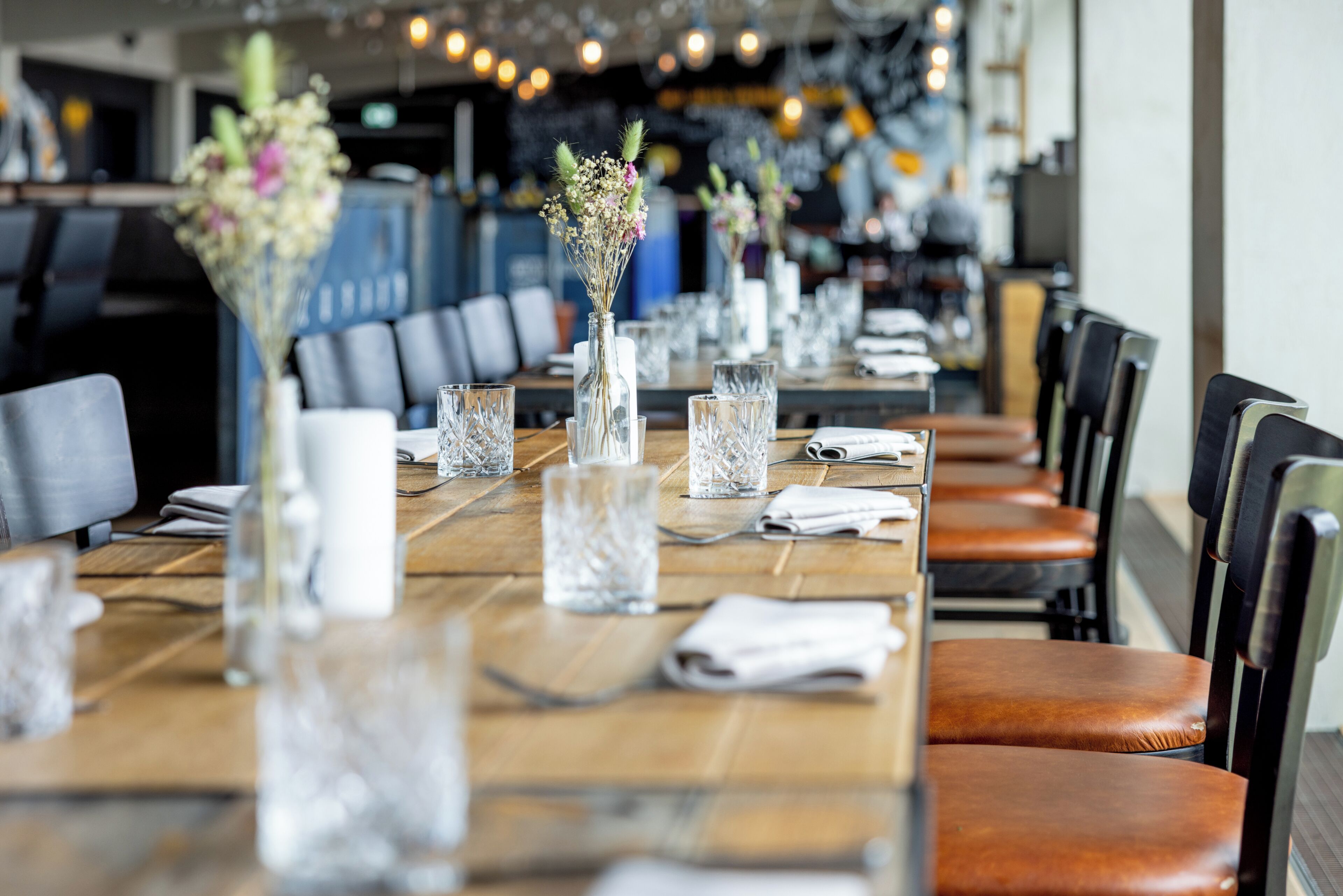 A restaurant with long wooden tables, clear glassware, and vases with flowers.