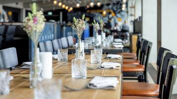 Un restaurante con mesas de madera largas, copas de vidrio transparentes y jarrones con flores.