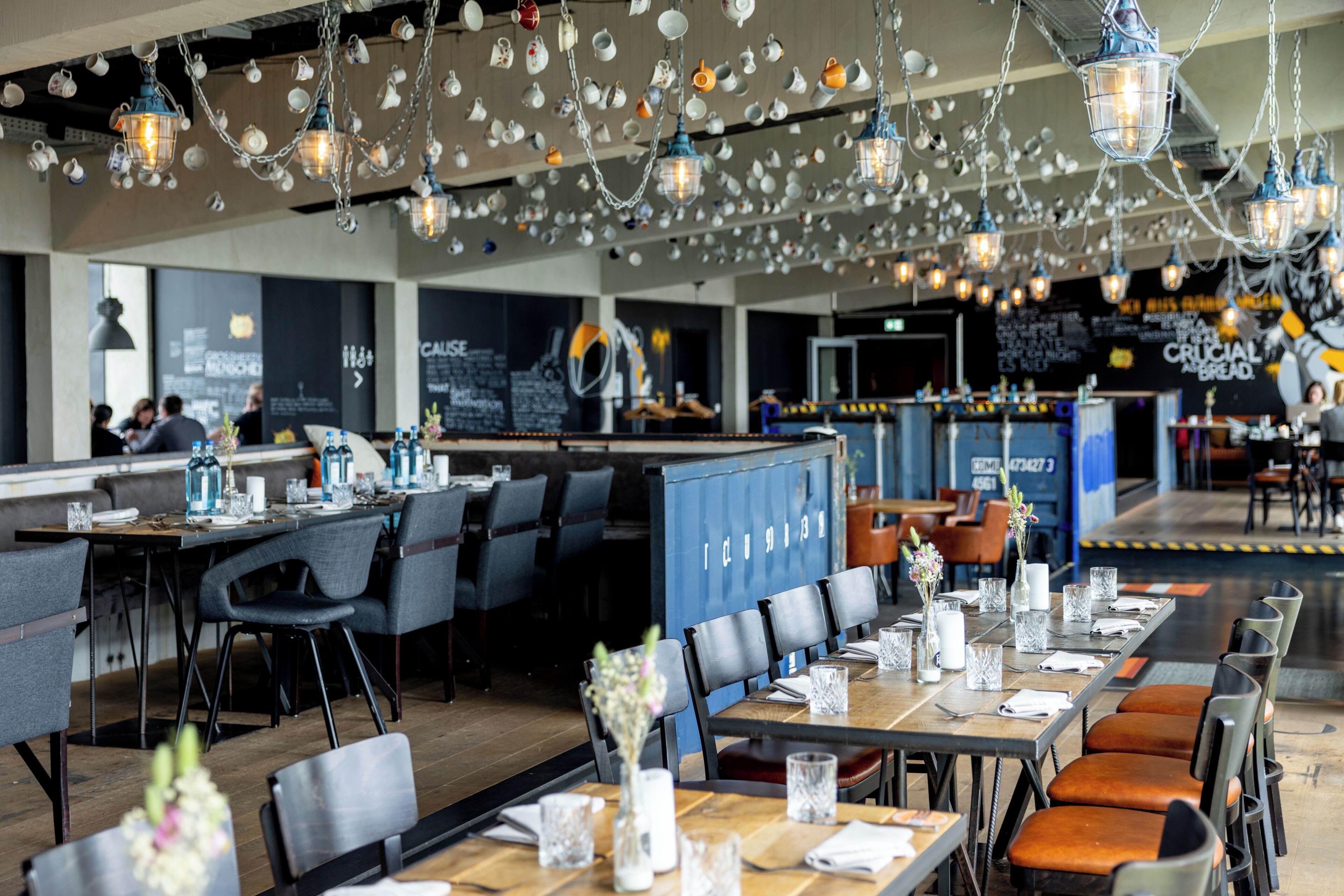 A restaurant with tables set for dining, hanging light fixtures, and a counter area.
