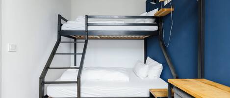 A bunk bed with a wooden ladder, a wooden bench, and a small wooden table with drawers.