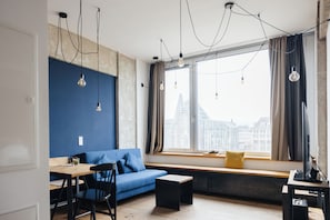 Un espace de vie moderne avec un mur bleu, une table en bois, un canapé et une fenêtre donnant sur la ville.