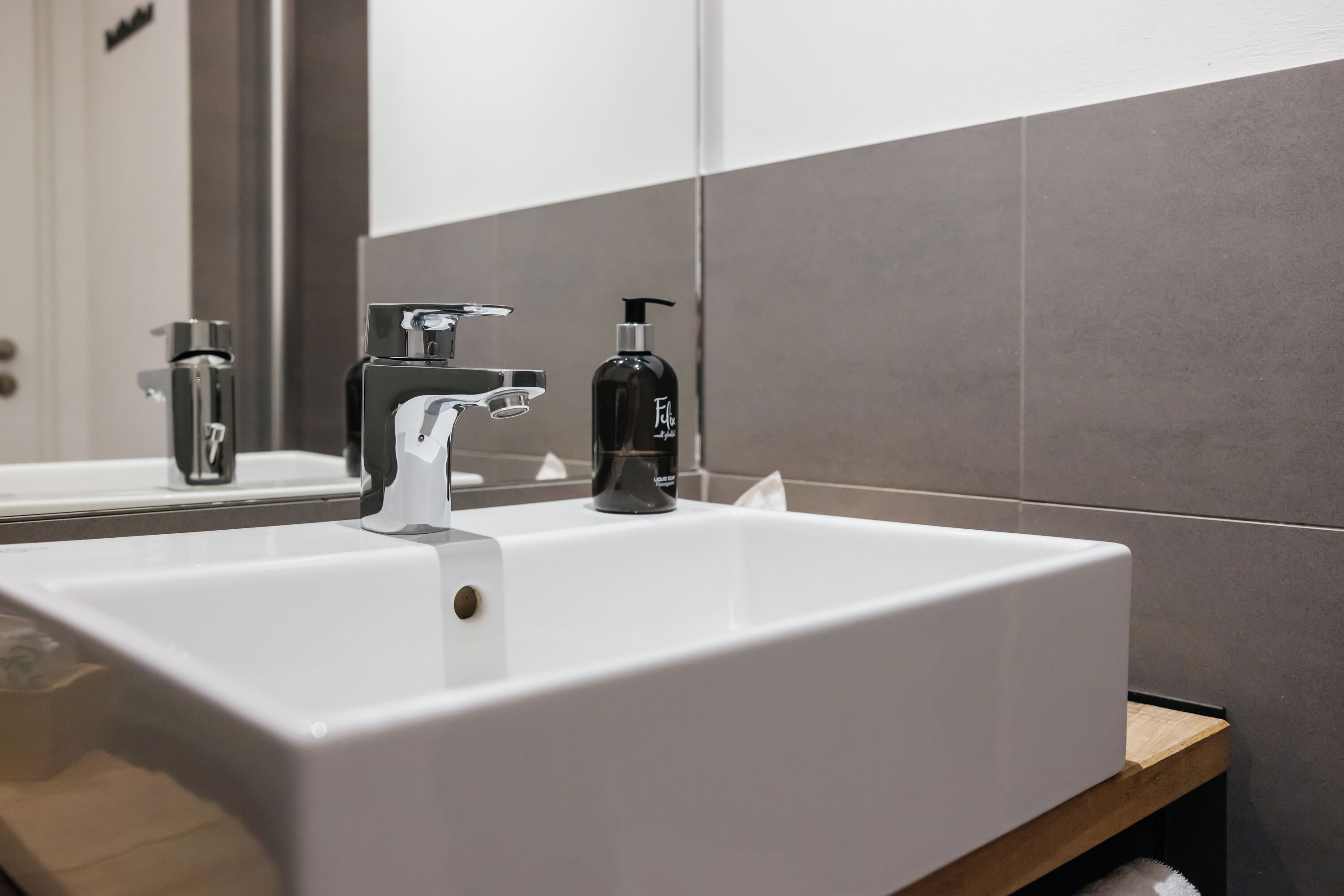 A bathroom with a white sink, a modern faucet, and a black soap dispenser.