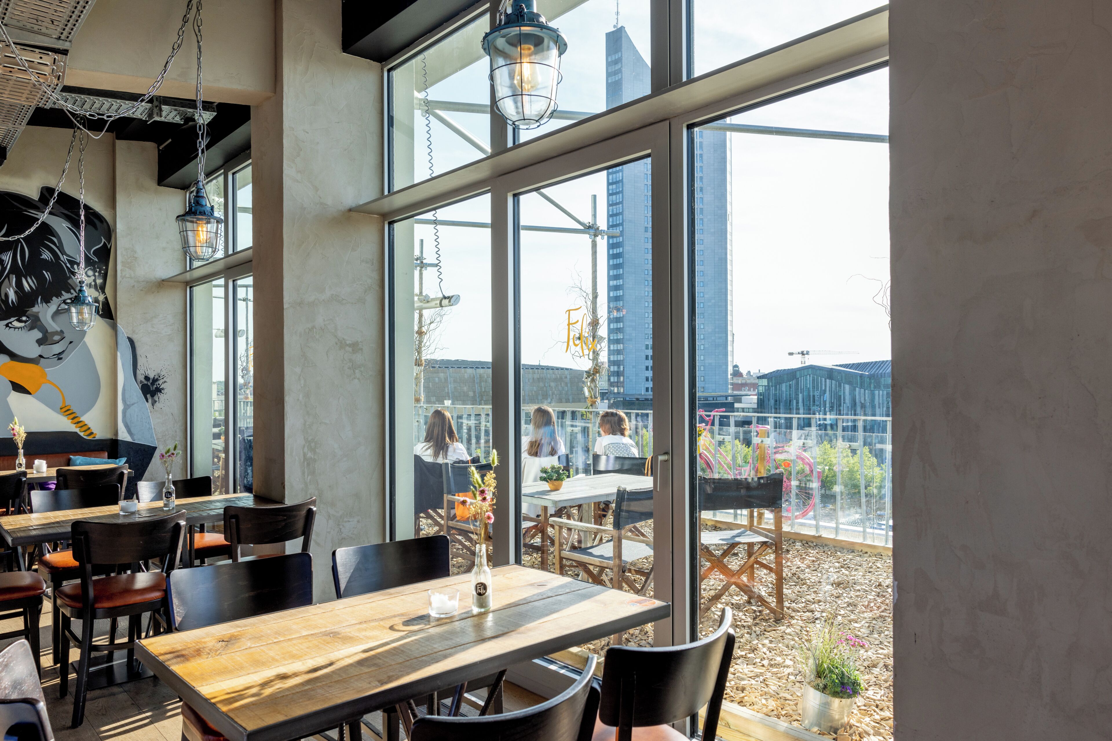 An indoor dining area with large windows, wooden tables, and chairs.